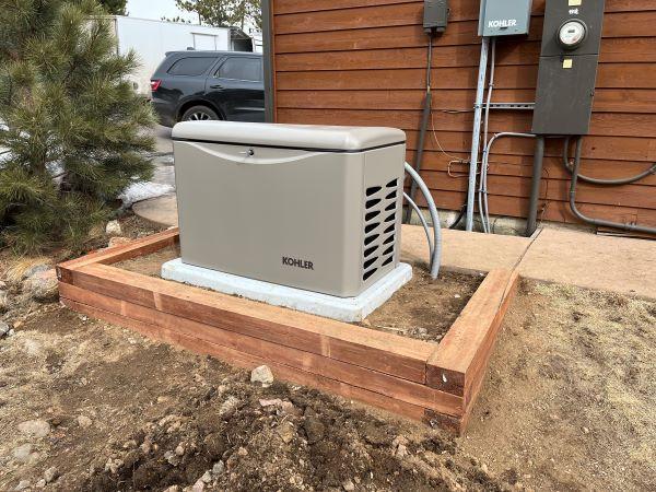 grey Kohler home generator on a wooden platform behind a wooden house